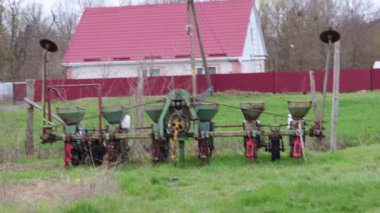 Yeşil paslı tarımsal tohum ekiciler yemyeşil çayırlarda, yıpranmış çiftlik evinin yanında, yakınlardaki kırmızı çatılı ahşap çitin yanında dinleniyor.