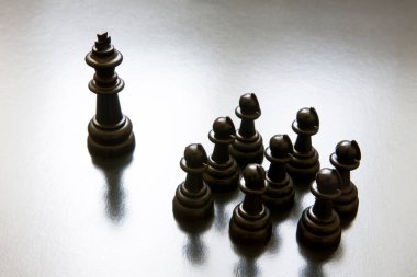 Kral figürü piyonların karşısında duruyor. Siyah bir arkaplanda satranç taşları.