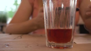 Yakın plan. Şehirdeki bir kafede şeffaf bir bardağa kırmızı komposto dökülüyor, bir kızın arka planına karşı. Sıvı, kabarcıklar. Yavaş çekim