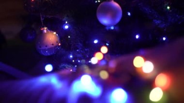 Yüzen odak, önden arkaya doğru. Yılbaşı arkaplanında, karanlığın içinde Noel, toplar, oyuncaklar ve çelenklerin çok renkli yanıp sönen ışıkları. yakın plan