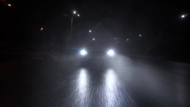 車は高速道路のアスファルトの道路で大雨の夜に運転している ヘッドライトは雨の中輝きます ヘッドライトからの光のビームバンパーの前の車の眺め — ストック動画