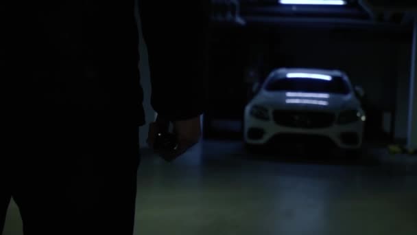 一个男人的轮廓 用汽车钥匙拍手的特写 在地下停车场的黑暗中关掉警报 前灯亮着 — 图库视频影像