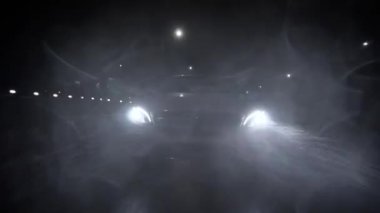The car is driving at night in heavy rain on an asphalt road at high speed. Headlights shine through the rain. A beam of light from the headlightsView of the car in front of the bumper