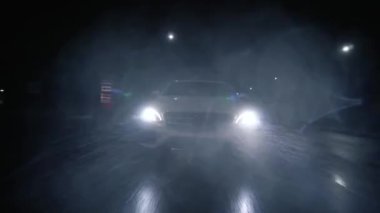 The car at high speed, at night, travels along the road in the city. Headlights on. Beam of light through the downpour, drops