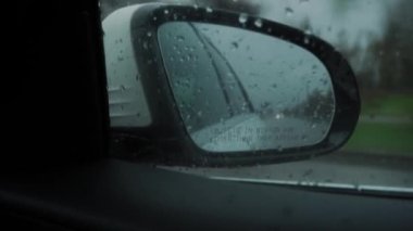 Close-up. Blind Spot Monitor Lights up on the side mirror of the car when overtaking, while driving on the road in the rain