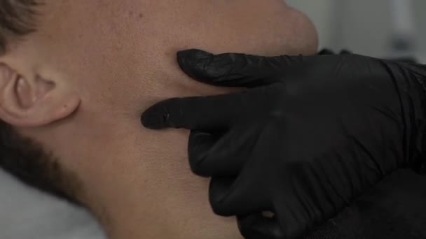 黒手袋で手のクローズアップ 医者はオフィスで美容整形の後男の顔の皮膚をマッサージ — ストック動画