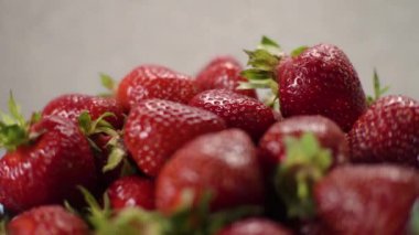 Kameraya bak, bulanık. Tam mavi sepet, tabak, vazo, kap, mutfakta taze kırmızı, yeşil çilekler, gri, beyaz arka planda. Makro. Işıktan parla