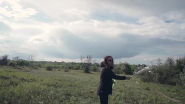 Dışarıda sabun köpüğü üfleyen güzel genç bir kız. Çocukluğun yavaş çekim videosu yetişkinliğe dönüşüyor. Güneş ışınları altında eğlenmek. Gün doğumu. Baloncuklara odaklan.