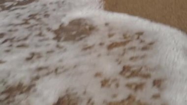 slender beautiful female legs walk along the wet warm sand on the Black Sea coast, leaving deep footprints. waves crashing, filming from behind, close-up
