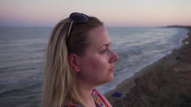 Kafasına gözlük takmış, çok renkli elbiseli bir sarışın düşünceli bir şekilde kameraya doğru üzgün bir şekilde bakar ve etrafa ateş eder. Güzel pembe bir günbatımının ardında, ılık Karadeniz