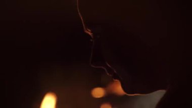 Yakın çekim silueti, genç, uzun saçlı, yalnız bir kız. Doğa, ateşin yanında, deniz sahilinde, gece. Kız akıllı telefondan mesajları karıştırıyor. Ilık arka ışık, ateşten. Arkaplanda