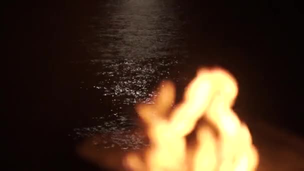 夜はキャンプファイヤーでバーベキューグリルが燃える 遠くの計画への焦点の変更は 海への月明かりのパスには ビーチ 闇の水波 手持ち — ストック動画