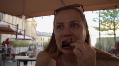 Kapalı bir yüz, aç bir kız, uzun saçlı, güneş gözlüklü, aç gözlü, hızlı, iştahlı, iştahlı, aç gözlü, şişman eti yiyen, pirzola yiyen. Bir kafede et kemiği tutuyor, sokağın karşısındaki restoranda..