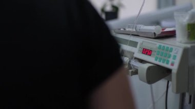 Hastanedeki tıbbi monitör. Ameliyat odasında mavi üniformalı doktorların arka planında modern ekipmanlar var. Ekranda hastaların hayati belirtileri görülüyor.
