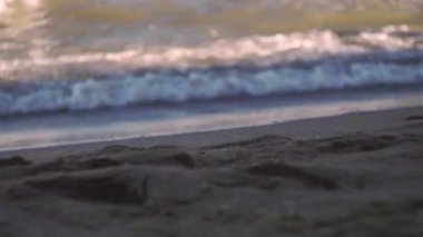 Denizin arka planında sakin dalgalarla kumlu bir sahil. Tripodla ateş etmek. Dalgalara odaklan. İyi günler. Yaz