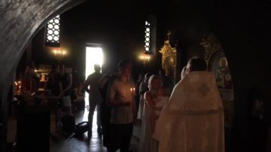 Kyiv, Ukrayna - 08 Temmuz 2021: Siyah sakallı rahip cüppeli beyaz cüppeli küçük kızı annesinin kollarında vaftiz ediyor, vaftiz ailesi yakınlarda duruyor, elinde mumlar, tüm aile dikkatlice izliyor,