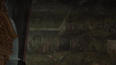 Kilisenin alacakaranlığında, duvardaki azizlerin eski bir simgesini vurmak.