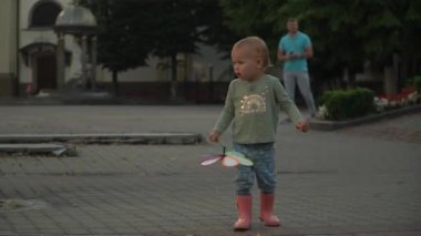 Yaramaz kız lastik botlar, oyuncak fırıldak, yel değirmeni, yakın çekim çocuk ayakları su sıçratıyor. Saf ve basit mutlulukları yakalamak çocukluğun büyülü yağmurlu günlerini yakalamak. Gün, şehir