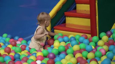 Küçük güzel kız tişörtü bilardo topları çocuk parkında oturur ve sırayla renkli topları alır onları uzağa atar, adımlarını temizler, sıcak yaz günü, çocukluk, neşe, neşe