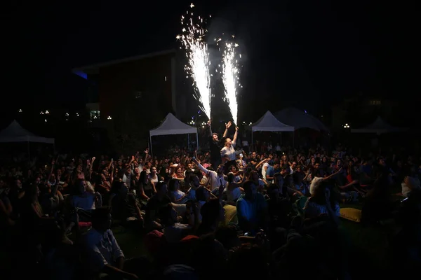 İnsanlar konserde eğleniyor ve gençler meşale yakıyor.