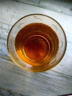 Altın sıvıyla dolu berrak bir bardak öğleden sonra güneş ışığının sıcacık parıltısını yakalar, kırsal bir cazibe ve derinlik katan ahşap bir yüzeyde dinlenir..