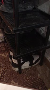 Siyah beyaz bir çift ayakkabı siyah bir rafa yerleştirilir, küçük bir odada düzenli ve düzenli bir görünüm oluşturur..