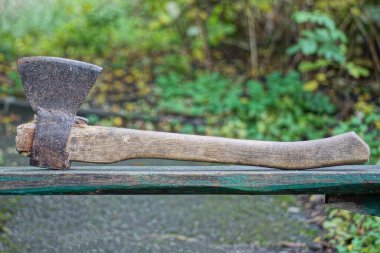 Gri, büyük, tahta saplı demir bir balta. Sokakta bir masanın üzerinde duruyor.