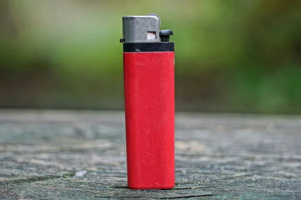 one red old plastic lighter stands on a gray table