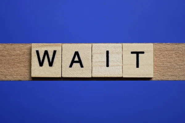 stock image word wait made from wooden gray letters lies on a blue background