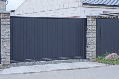 Gri tuğlalardan ve sokaktaki demirden yapılmış bir çitin duvarındaki siyah büyük metal kapı.