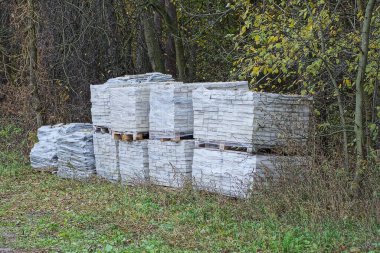 Sokaktaki yeşil çimlerin ve bitkilerin üzerinde duran tuğlalarla plastik ambalajlı kare kutular üzerinde sıra sıra dizilmiş.