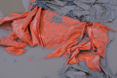 Caddedeki gri su birikintilerindeki kırmızı, kirli, buruşuk selofan parçasının plastik dokusu.