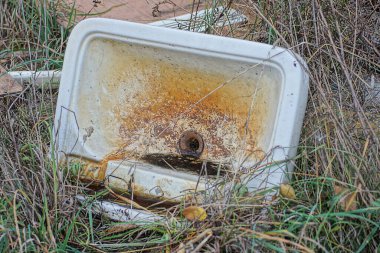 Beyaz, eski bir seramik lavabonun çöpü kahverengi toprakta duruyor yeşil ve gri kuru çimenler arasında sokakta.