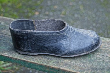 Eski, kirli, siyah bir galoş ayakkabısı, sokaktaki gri ahşap bir masada duruyor.