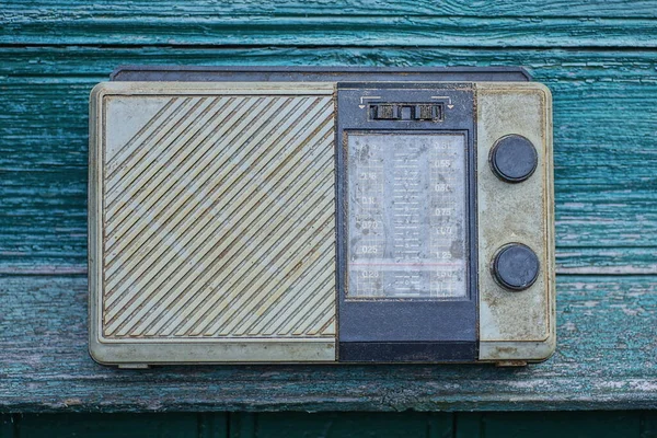 一个旧的 肮脏的 灰色的 黑色的塑料收音机靠在一张绿色的木头墙上的桌子上 — 图库照片