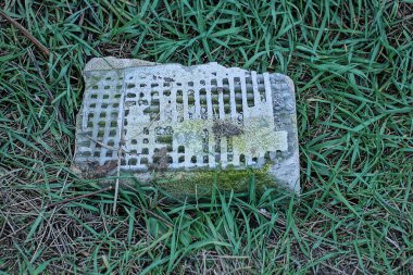 one gray concrete piece lies on the ground in the green grass on the street