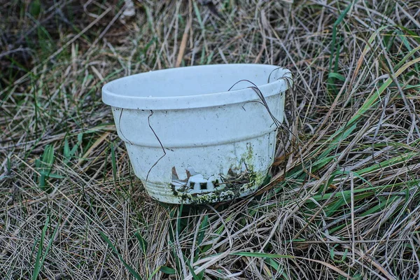 garbage from one white broken plastic flowerpot with a crack lies on the ground and green grass in nature
