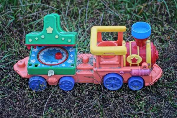 one colored large plastic toy train stands on the grass and earth on the street