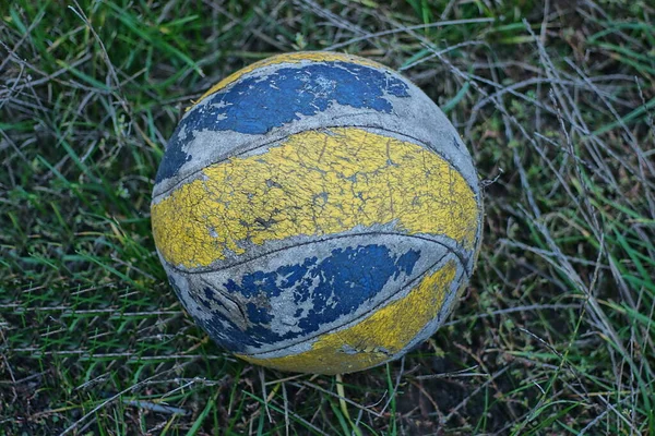 古いみすぼらしい革の青い黄色のバレーボールが通りの緑の草の中にあり — ストック写真