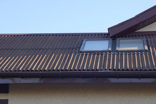 茶色のスレート屋根の民家の屋根裏部屋青い空に向かって通りに2つの窓 — ストック写真