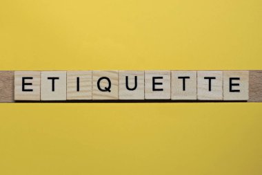 Gri küçük ahşap harflerin görgü kuralları sarı bir masada yatıyor.