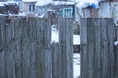 Kırsal bir sokakta beyaz karın arka planında kırık ahşap tahtalar olan eski gri bir çit duvarının parçası.