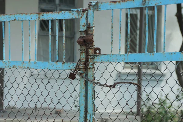 街上用褐色锈迹斑斑的铁网封闭的蓝色金属门的一部分 — 图库照片