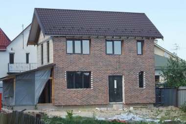 Pencereleri ve çatısının altındaki gri gökyüzüne karşı bir kapısı olan büyük bir özel evin kahverengi tuğla cephesi.