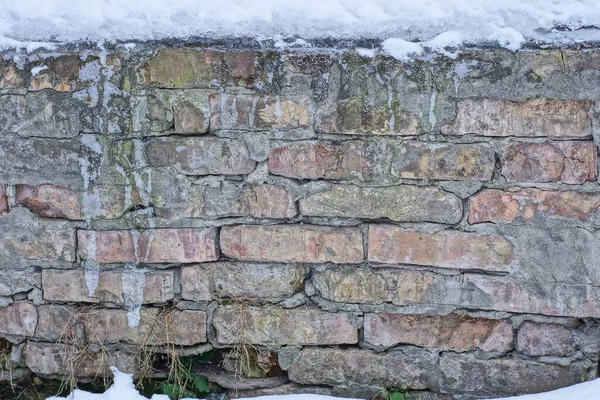 Kış sokağındaki beyaz karlı eski kahverengi bir duvarın taş dokusu.