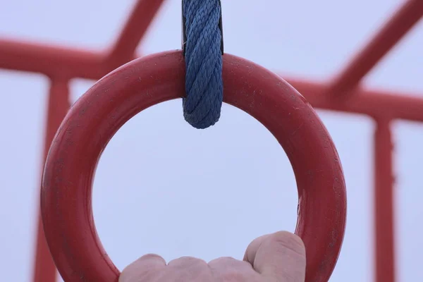hand hold one red metal sports ring hangs on a blue iron cable outdoors at a construction site