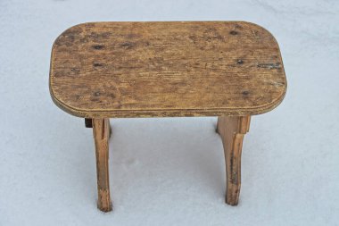 Eski, kahverengi, ahşap bir tabure kış sokağındaki beyaz karda duruyor.