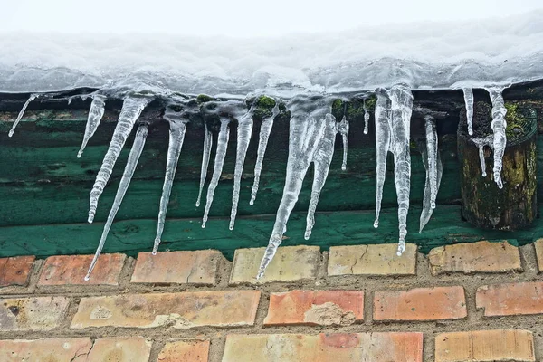 white snow and a row of icicles on the roof of a brown brick house on a winter street