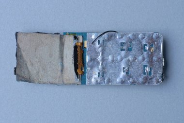 Parçalanmış eski bir cep telefonunun parçası gri bir masada yatıyor.