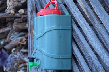 Kırmızı kapaklı bir plastik yeşil mobil yıkama tezgahı ve küçük bir musluk dışarıdaki gri ahşap duvarda asılı.